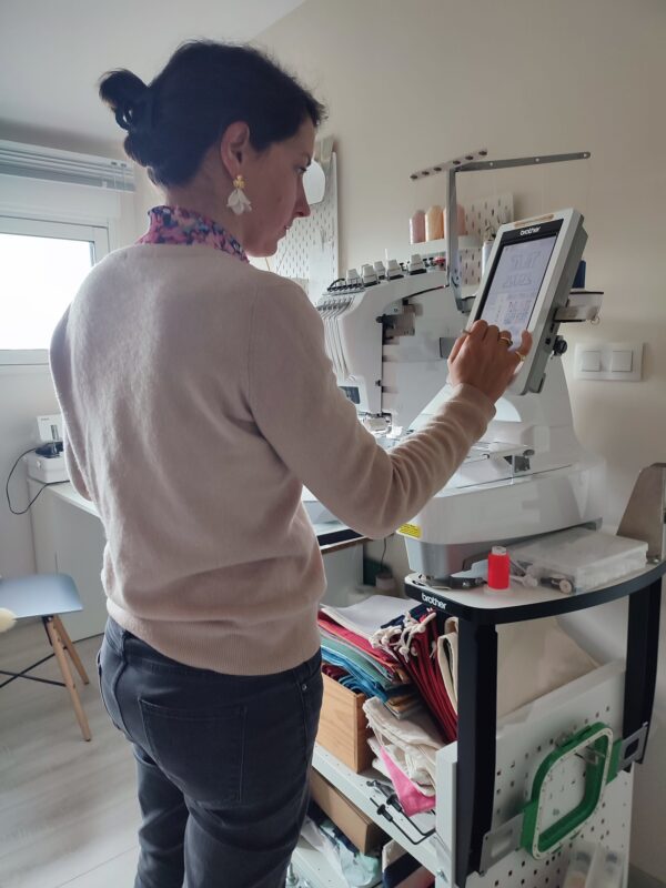 Charlotte créatrice de Maison de Camaret devant sa brodeuse PR655 Brother