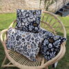 Coussin jacquard français Mage motif floral folk noir et écru passepoil doré fauteuil rotin Maison de Camaret
