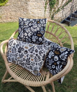 Coussin jacquard français Mage motif floral folk noir et écru passepoil doré fauteuil rotin Maison de Camaret